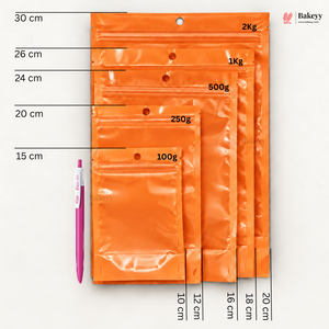 Five orange zip-top pouches in different sizes with printed weight labels (100g, 250g, 500g, 1Kg, 2Kg) and dimension markings in centimeters, shown on a white background with a pink pen for scale. A Bakesey logo appears in the top right.