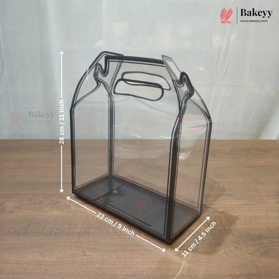 A clear plastic bakery gift bag or container with a handle, shown on a wooden surface with overlaid dimension lines and text indicating 23 cm by 23 cm by 11 cm.