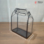 A clear plastic bakery gift bag or container with a handle, shown on a wooden surface with overlaid dimension lines and text indicating 23 cm by 23 cm by 11 cm.
