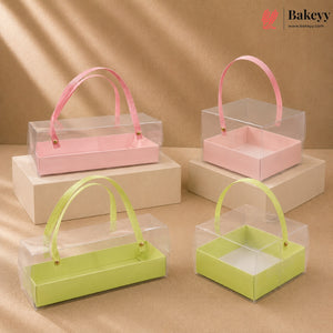 Clear gift boxes with pink and green handles on beige platforms, featuring the Bakeyy brand.