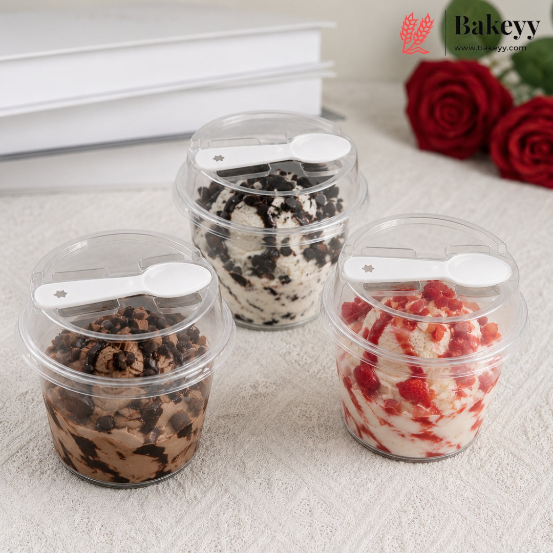 Three clear plastic tubs of frozen dessert or ice cream with lids and white spoons, arranged on a light textured surface. The tubs contain chocolate chip ice cream, cookie and cream ice cream, and strawberry ice cream.
