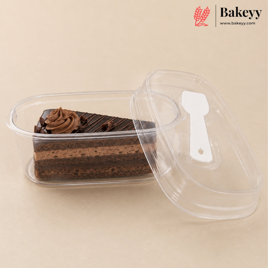 A clear plastic rectangular cake container holding a slice of chocolate cake with whipped cream, shown with its transparent lid leaning against it on a beige background. The Bakeyy logo appears in the top right corner.