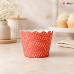 A single scalloped cupcake liner with a red and white polka dot pattern, standing on a light marble countertop in a softly blurred kitchen setting.