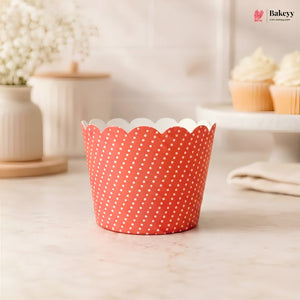 A single scalloped cupcake liner with a red and white polka dot pattern, standing on a light marble countertop in a softly blurred kitchen setting.