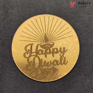 A round gold-colored metal plaque featuring an engraved diya and the words 'Happy Diwali' in cursive, displayed on a dark textured background. A 'Bakeyy' brand logo is visible in the top right corner.