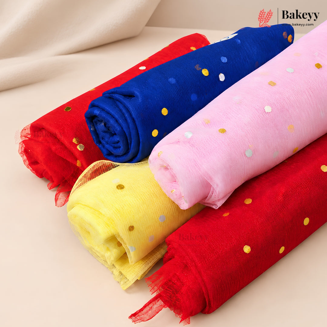 Four rolls of sheer mesh fabric in red, royal blue, pink, and yellow, each decorated with small metallic gold and silver confetti dots, arranged diagonally on a light beige surface.