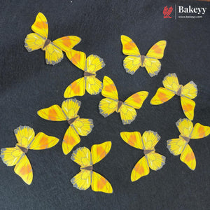 Nine yellow and orange butterfly-shaped decorative items arranged on a dark textured background, with a Bakeyy logo in the top right corner.