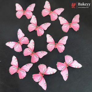 Nine pink butterfly-shaped cake toppers with gray vein details scattered on a dark gray background, with the Bakeyy logo in the top right corner.