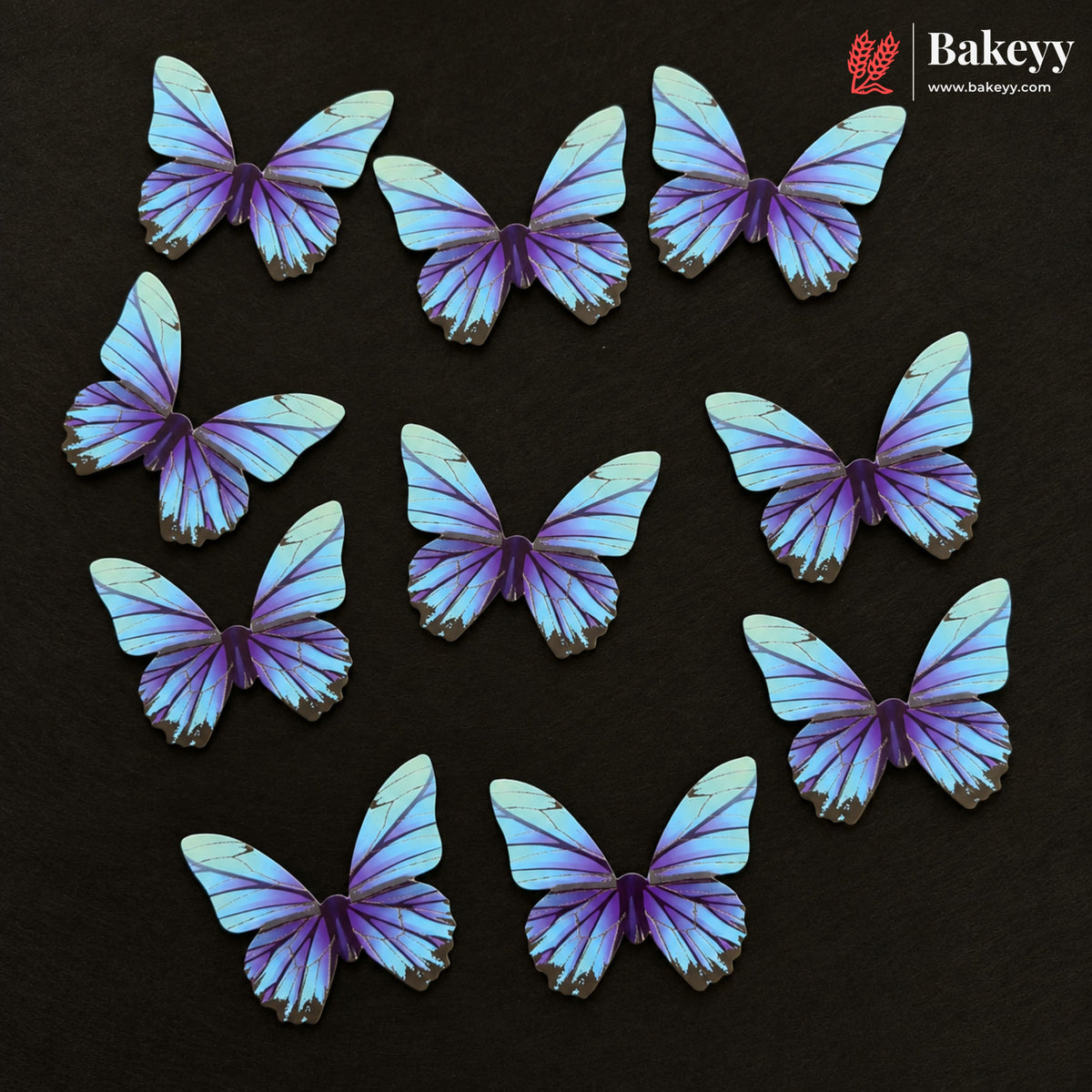 Ten butterfly-shaped cake toppers in shades of purple, blue, and white, arranged on a dark textured background. The Bakeyy brand logo is visible in the top right corner.