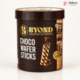 A dark brown plastic tub of BYOND Choco Wafer Sticks on a clean white background. The label features gold and white text, an illustration of two chocolate-coated wafer sticks, and a small kitchen scene on the right side.