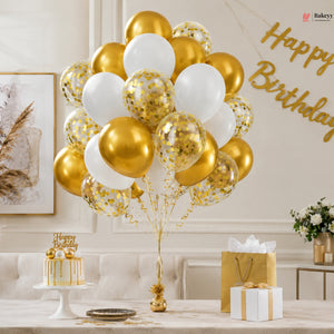 Birthday celebration setup with gold and white balloons, cake, and gift boxes.