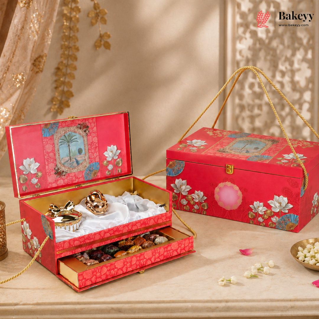 An ornate red gift box set for chocolates, shown open with gold-trimmed compartments holding assorted chocolates and sweets, alongside the closed matching box on a beige surface with decorative floral props.