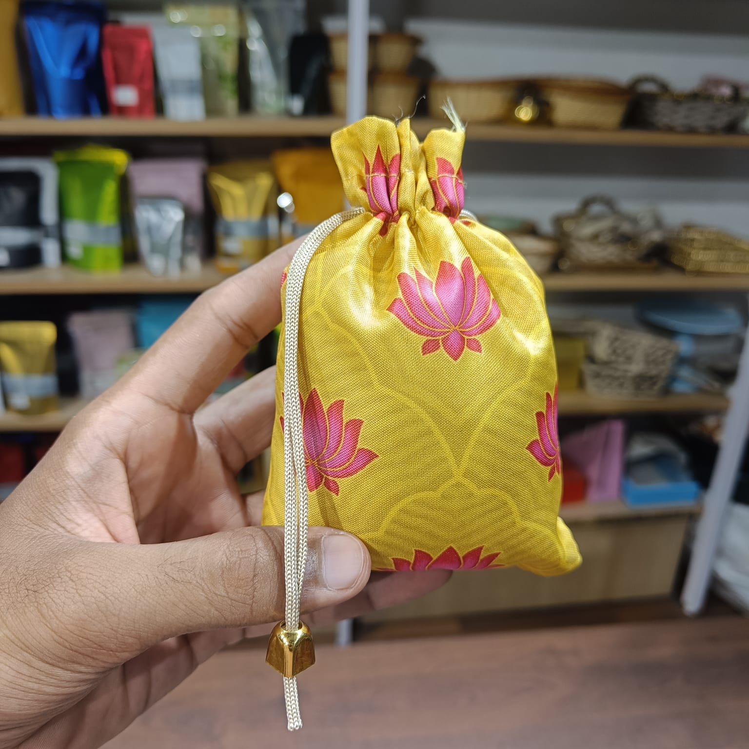 Yellow drawstring bag with pink floral patterns held by a hand in a store setting.