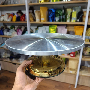 Metallic cake stand held in a hand with shelves of products in the background