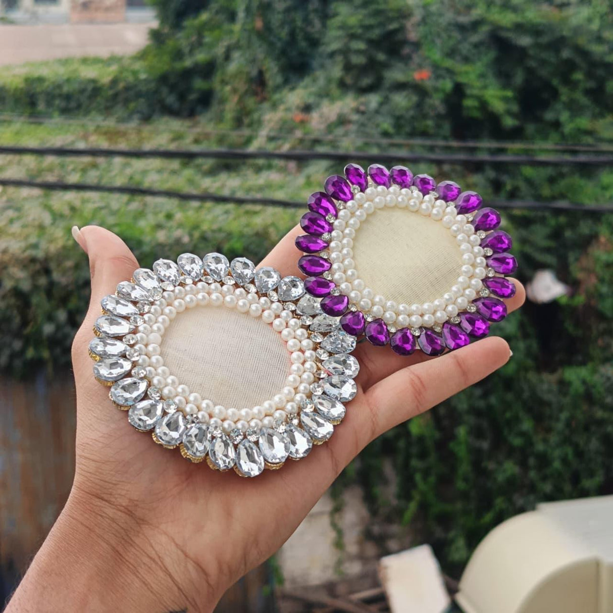 Hand holding two oval decorative brooch bases with pearls and rhinestones for gift packaging