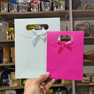 Two gift bags, one white with a blue bow and one pink with a red bow, held in front of a store shelf.