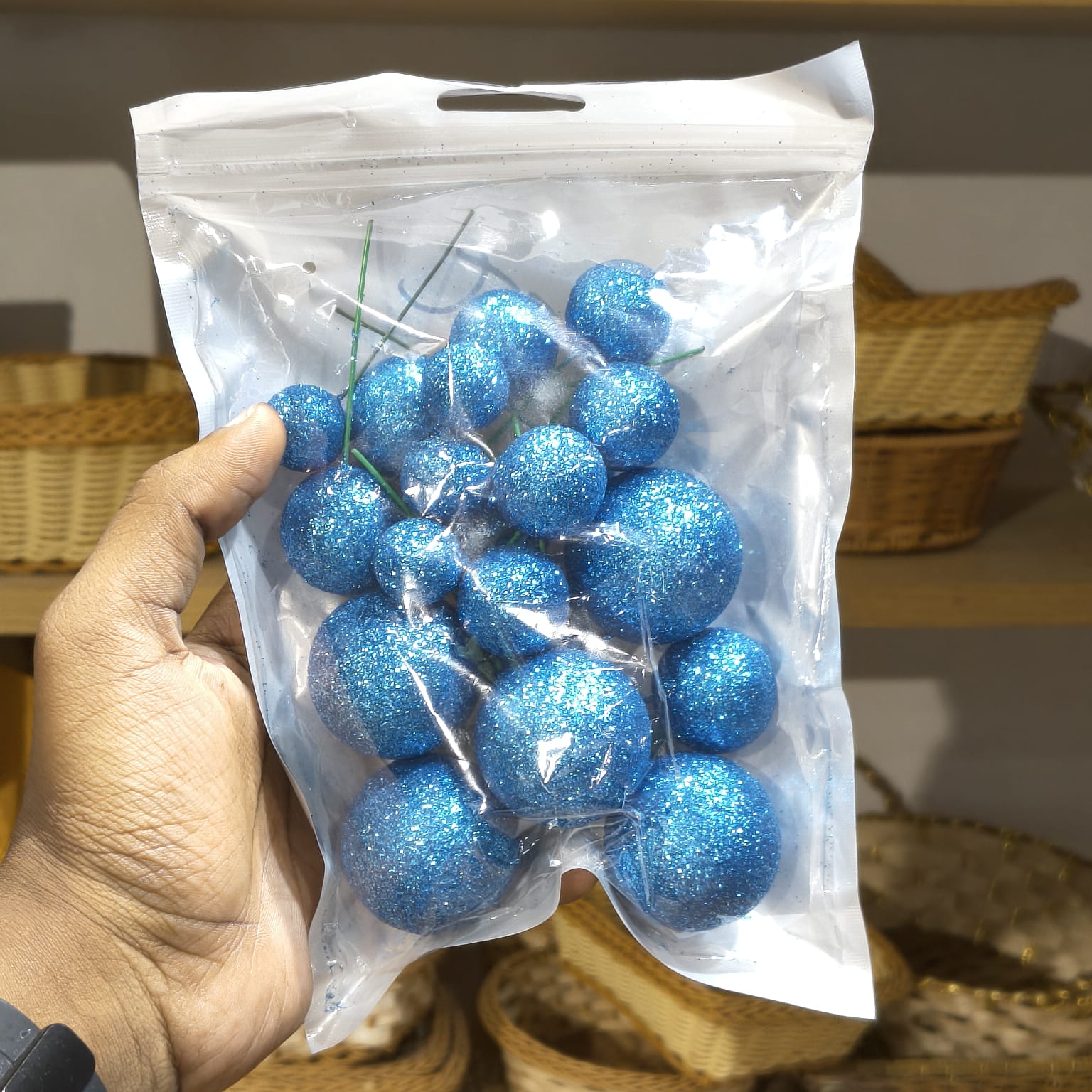 Hand holding a clear plastic bag with blue glittery balls against a neutral background