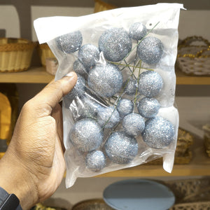 Hand holding a clear plastic bag with silver glittery balls against a blurred background