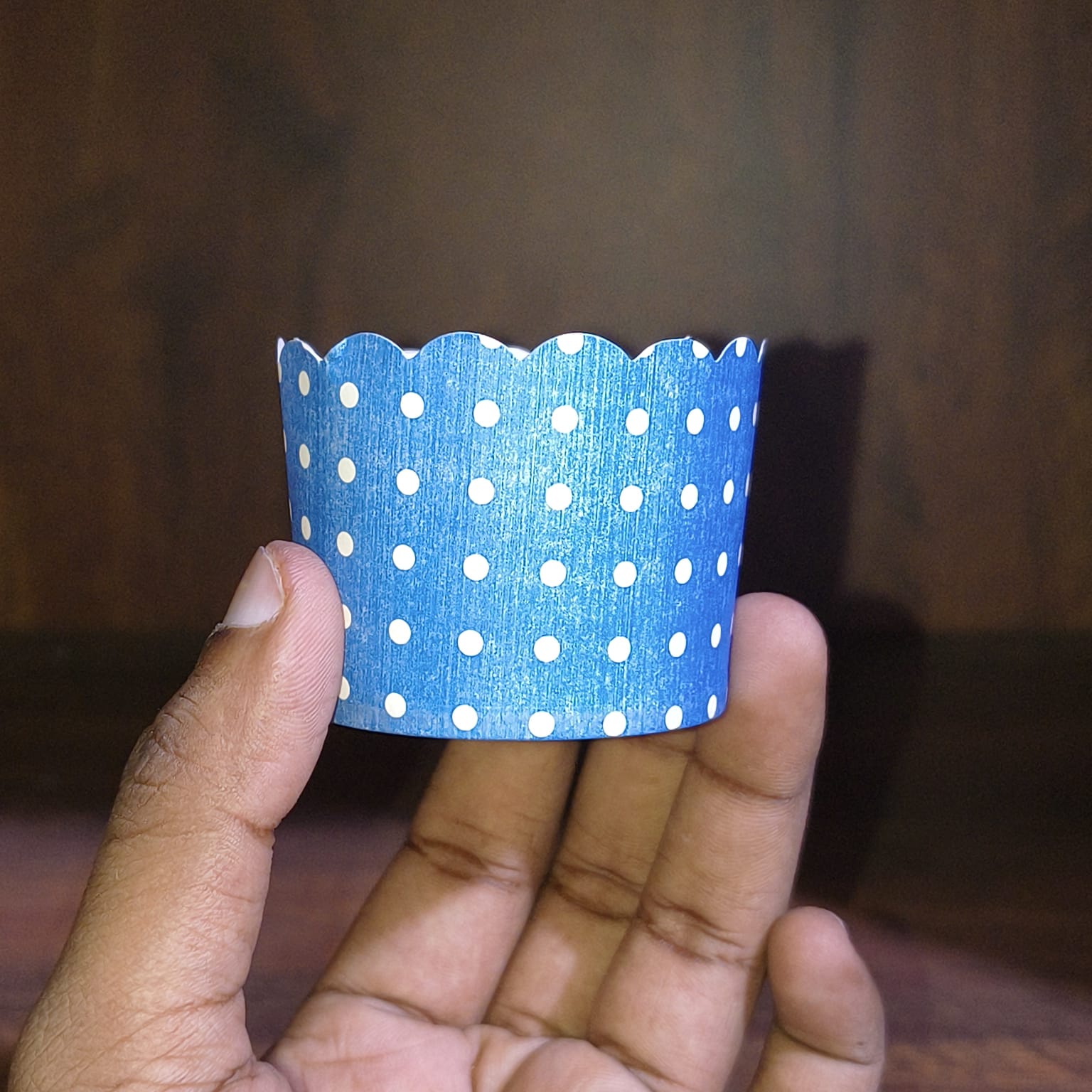 Hand holding a blue paper cup with white polka dots against a wooden background