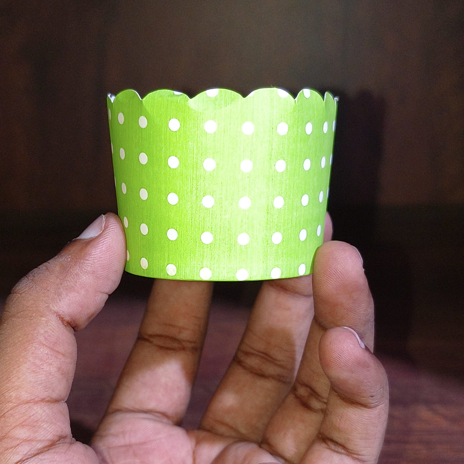 Hand holding a green paper cup with white polka dots against a dark background