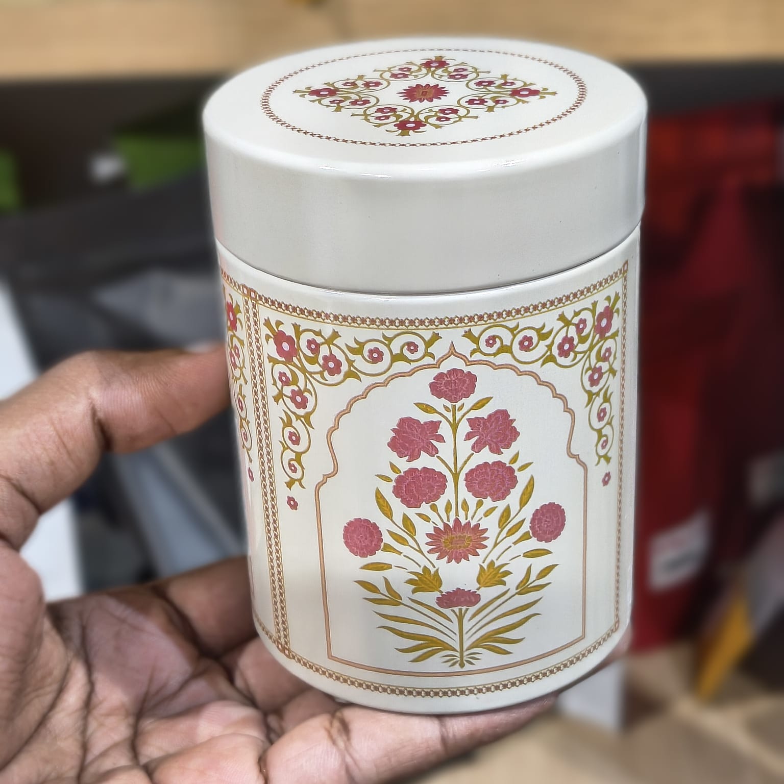 White cylindrical container with floral design held by a hand against a blurred background