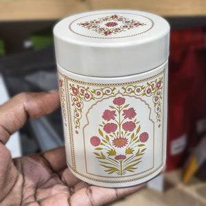 White cylindrical container with floral design held by a hand against a blurred background