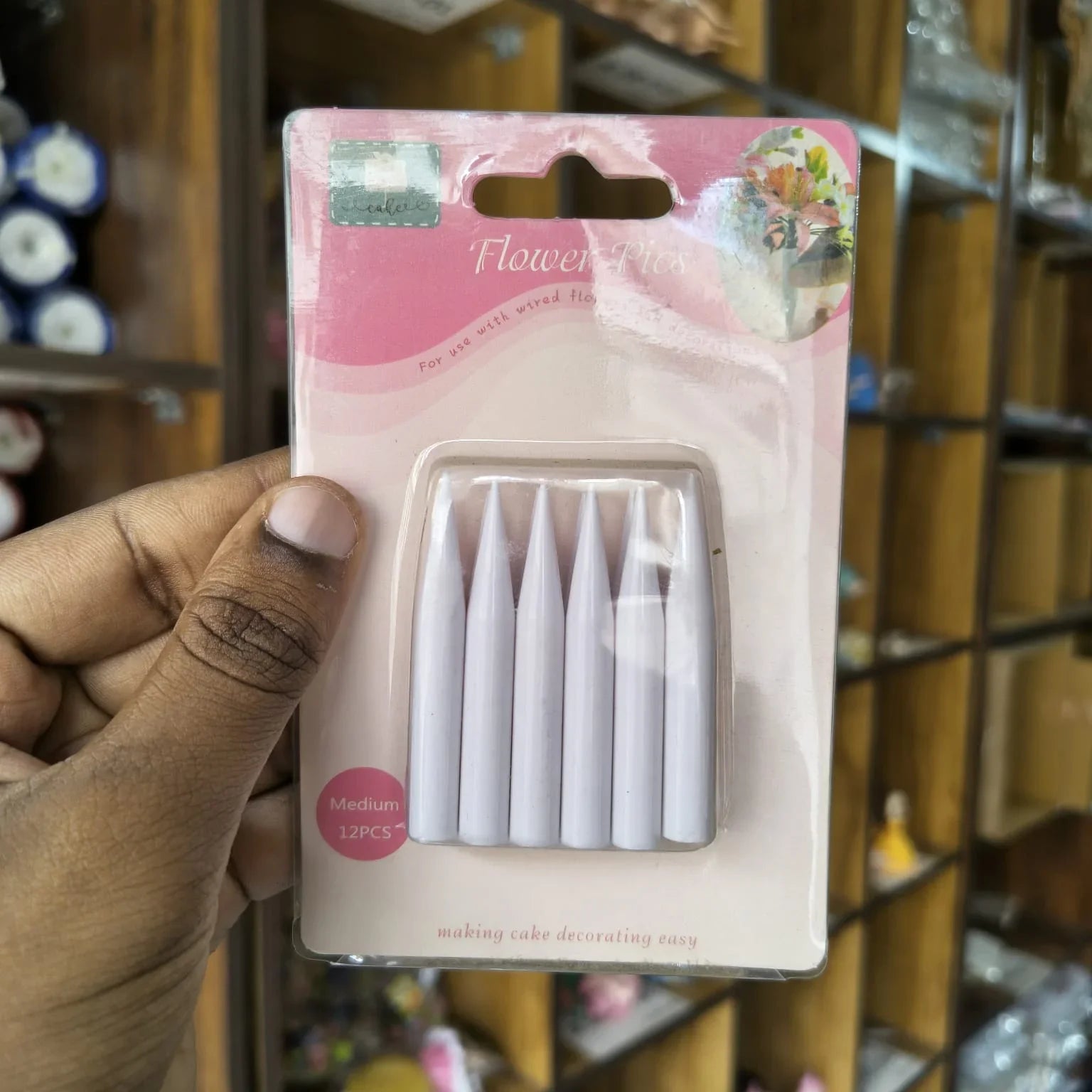 A hand holding a blister pack of five white cake decorating tips against a blurred shop background.