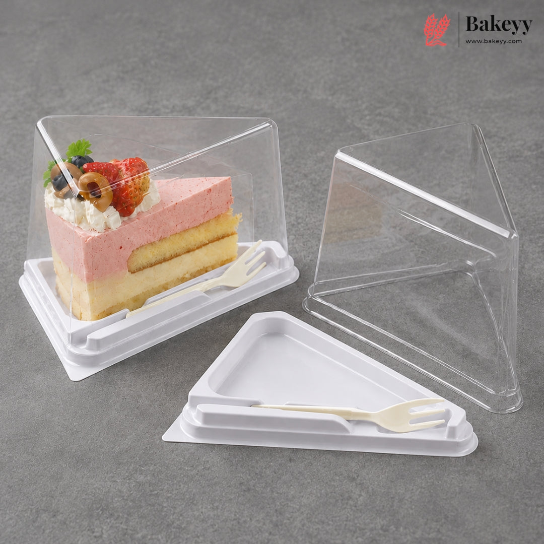 Clear plastic triangular cake box with a white base and small white plastic fork, shown both filled with a layered pink and yellow cake slice and empty on a gray surface. Bakeyy logo appears in the top right.