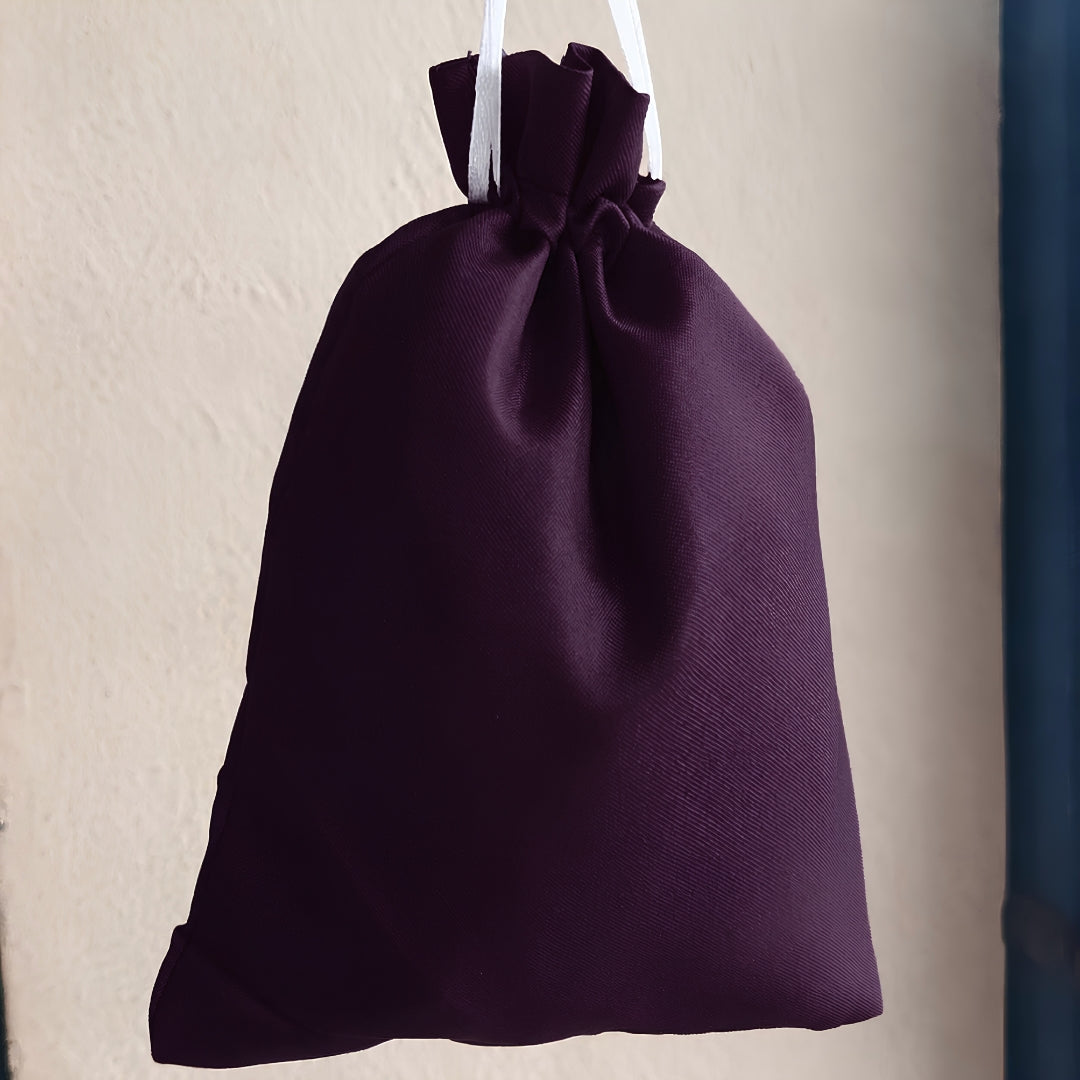 A dark purple drawstring pouch with white hanging strings, shown against a textured beige wall.