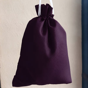 A dark purple drawstring pouch with white hanging strings, shown against a textured beige wall.