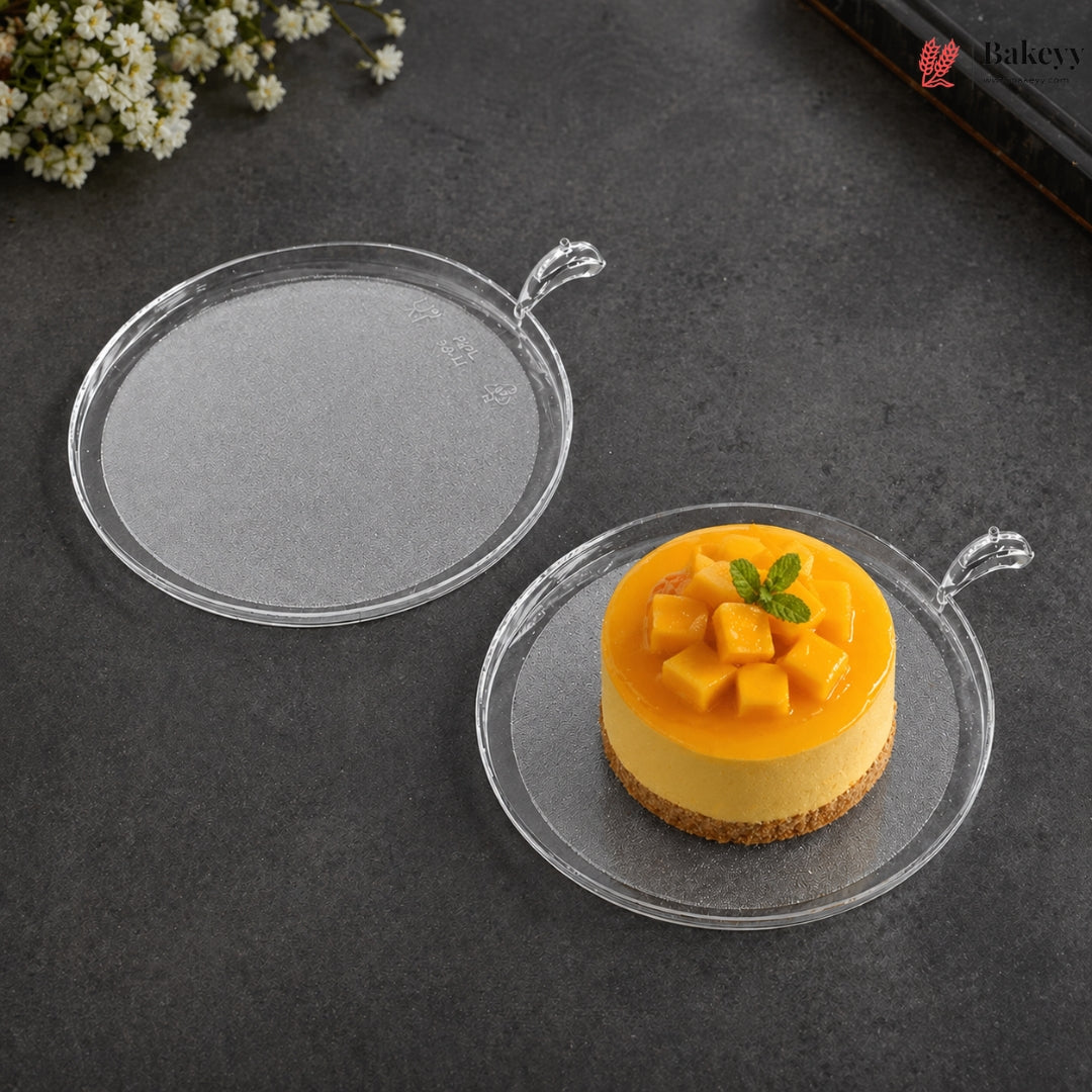 Clear round cake stand with a small yellow cake on a dark surface