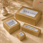 Gold boxes with 'YOUR LOGO' labels on a beige surface with a vase of dried flowers.