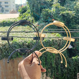 Hand holding black and gold metal diya stands, outdoor greenery in background, Bakeyy wholesale.