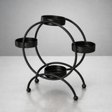 Black metal diya stand with four round holders for candles, displayed on a light surface