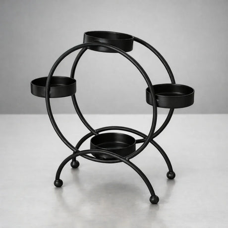 Black metal diya stand with four round holders for candles, displayed on a light surface