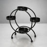 Black metal diya stand with four round holders for candles, displayed on a light surface