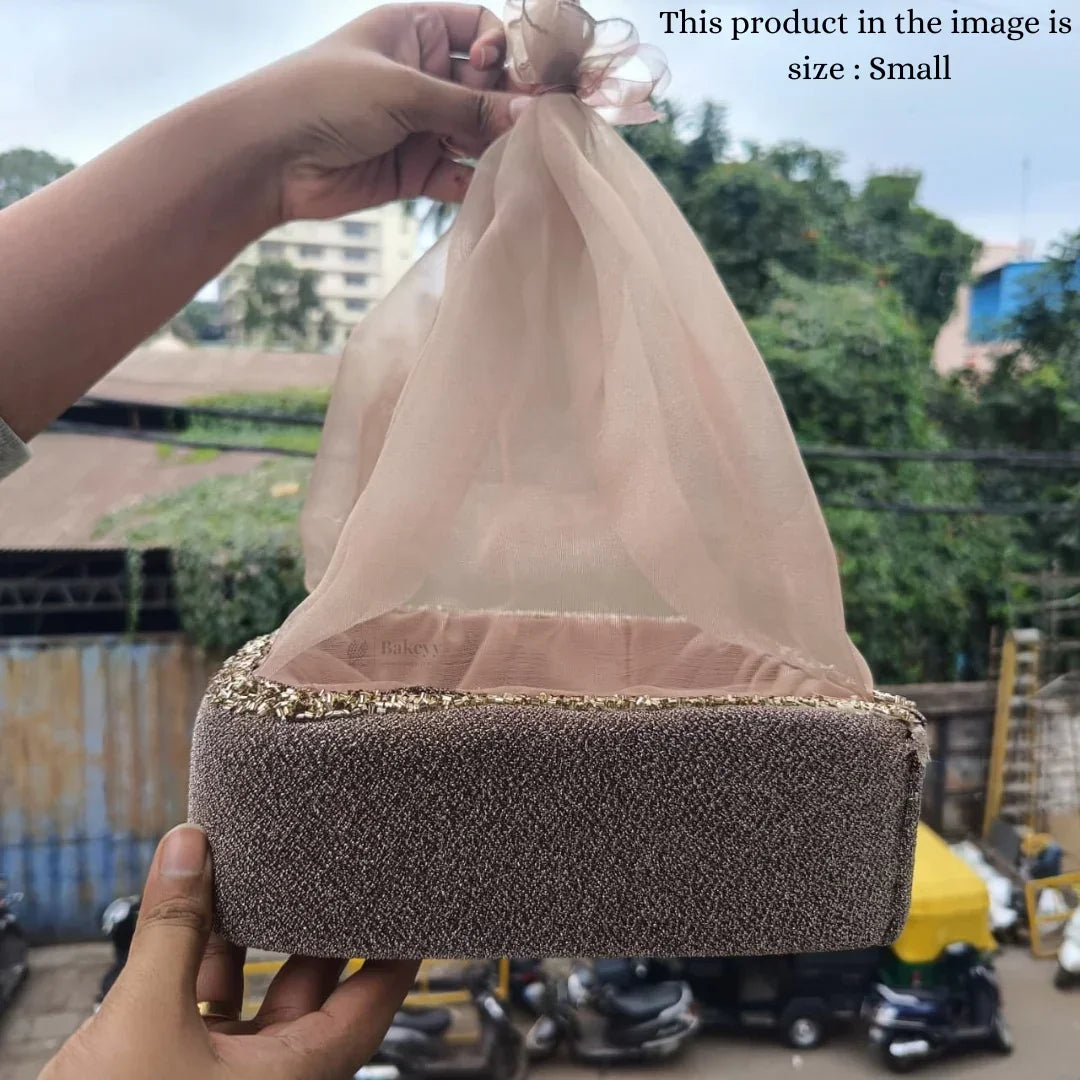 Small velvet gift hamper basket with net cover, held outdoors, Bakeyy hamper packaging.