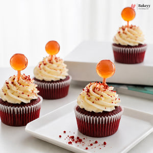 Red velvet cupcakes with cream cheese frosting and orange spherical decorations on a white plate.