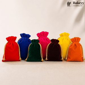 Velvet satin drawstring potli bags in multiple colors including red, blue, green, pink, maroon, yellow, and orange, arranged in a neat row on a soft beige fabric surface with a clean minimal cream background and gold cord detailing visible on each bag.
