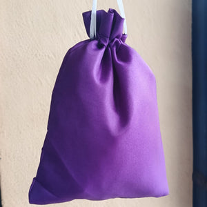Purple drawstring bag hanging against a beige wall