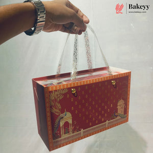 A red rectangular gift box with gold decorative patterns and illustrations of domes, held by a hand with a silver watch. The box has clear plastic handles and is photographed against a white background with a Bakeyy logo in the top right corner.