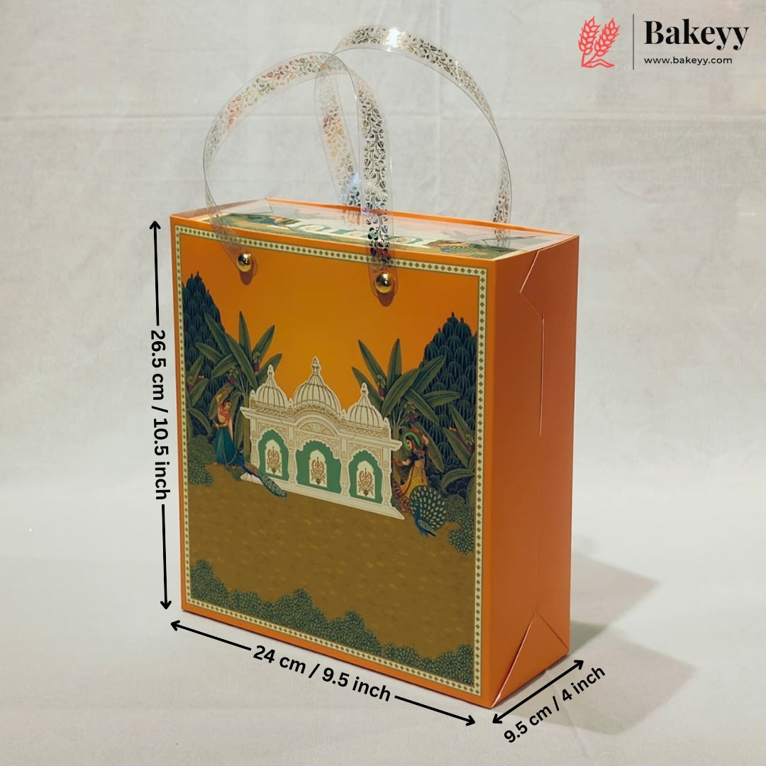 An orange bakery gift box with a printed illustration of a domed building and tropical foliage, shown with transparent handles and overlaid dimension lines indicating 26.5 cm height, 24 cm width, and 9.